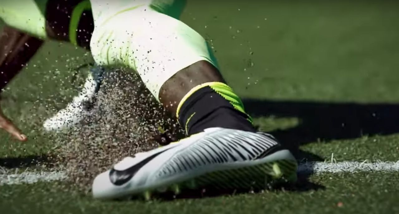 Leg and foot of football player wearing Nike cleat sliding and kicking up grass on football field