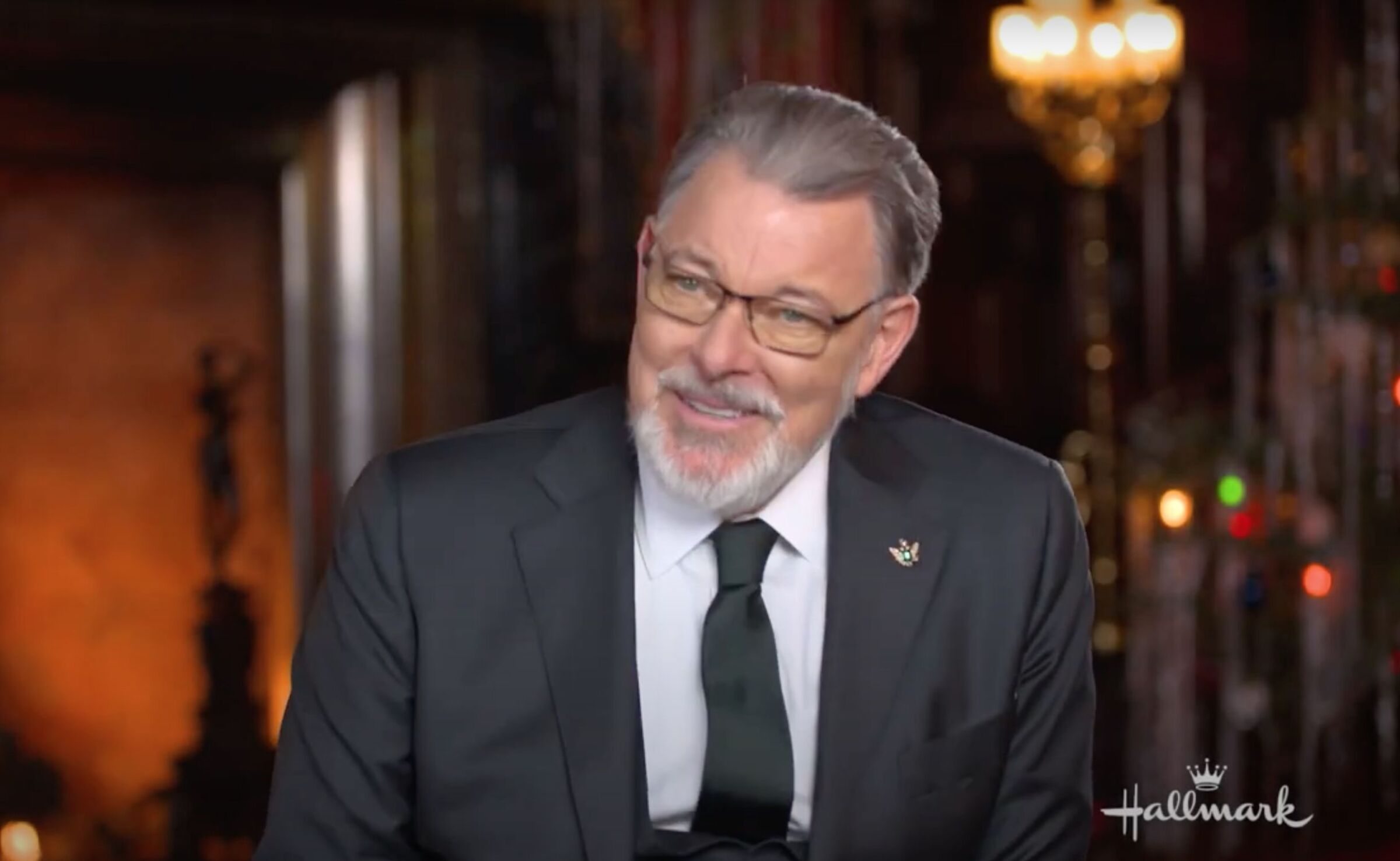 Actor from "A Biltmore Christmas" with beard and glasses wearing dark suit and tie