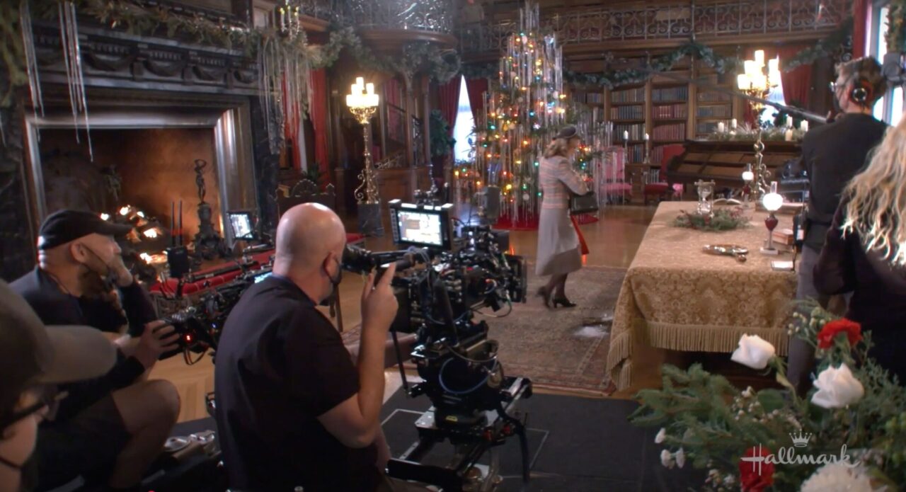 Behind-the-scenes view of movie crew filming female actor in a private library decorated for Christmas